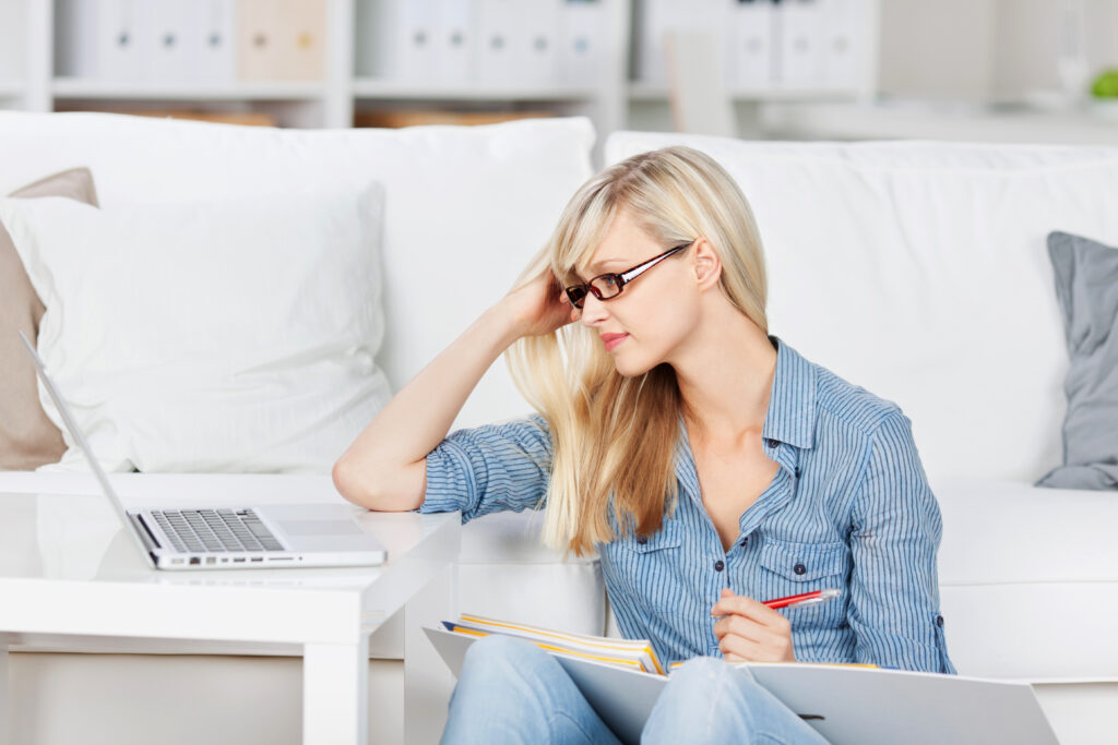 Blonde woman with glasses reviewing her lesson with her laptop and book